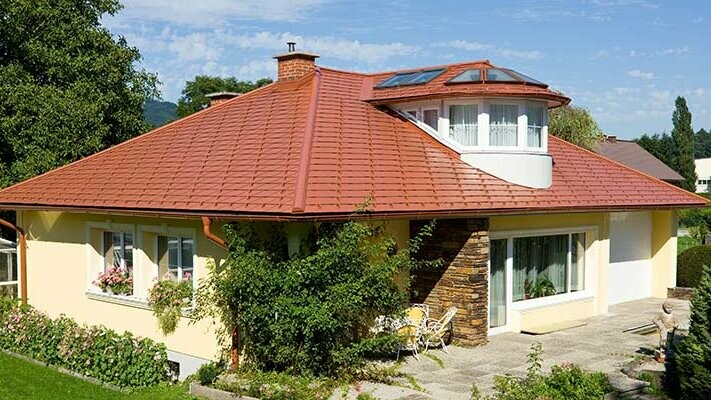 Maison individuelle avec toit à croupes et lucarne recouverte avec le bardeau PREFA en aluminium imitation tuile, rouge tuile.