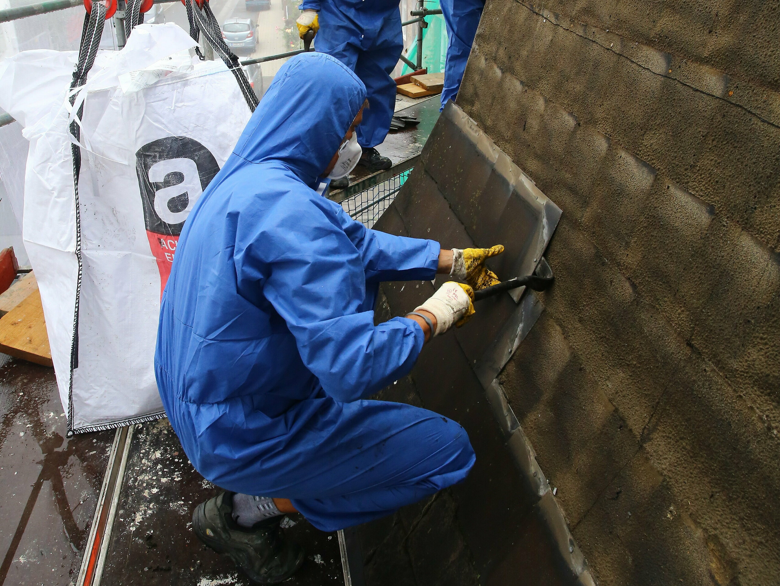 Geschulter Arbeiter beim Entfernen und Entsorgen der asbesthältigen, alten Dacheindeckung mit Mundschutz, um ein Einatmen des Asbests zu vermeiden