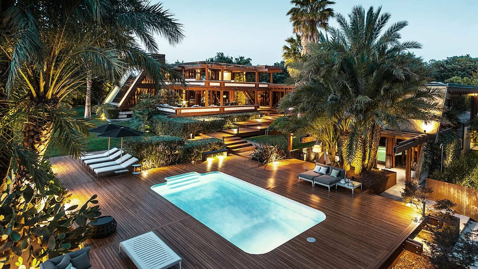 Weitwinkelansicht der Pagano-Anlage mit Pool und bequemen Liegeflächen. Palmen und indirektes Licht verleihen dem Ganzen ein luxuriöses Flair.