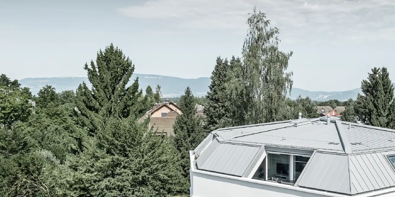 Semplice condominio con Prefalz PREFA in patina grigio; la facciata è realizzata con intonaco bianco con ampie logge all'angolo esterno.