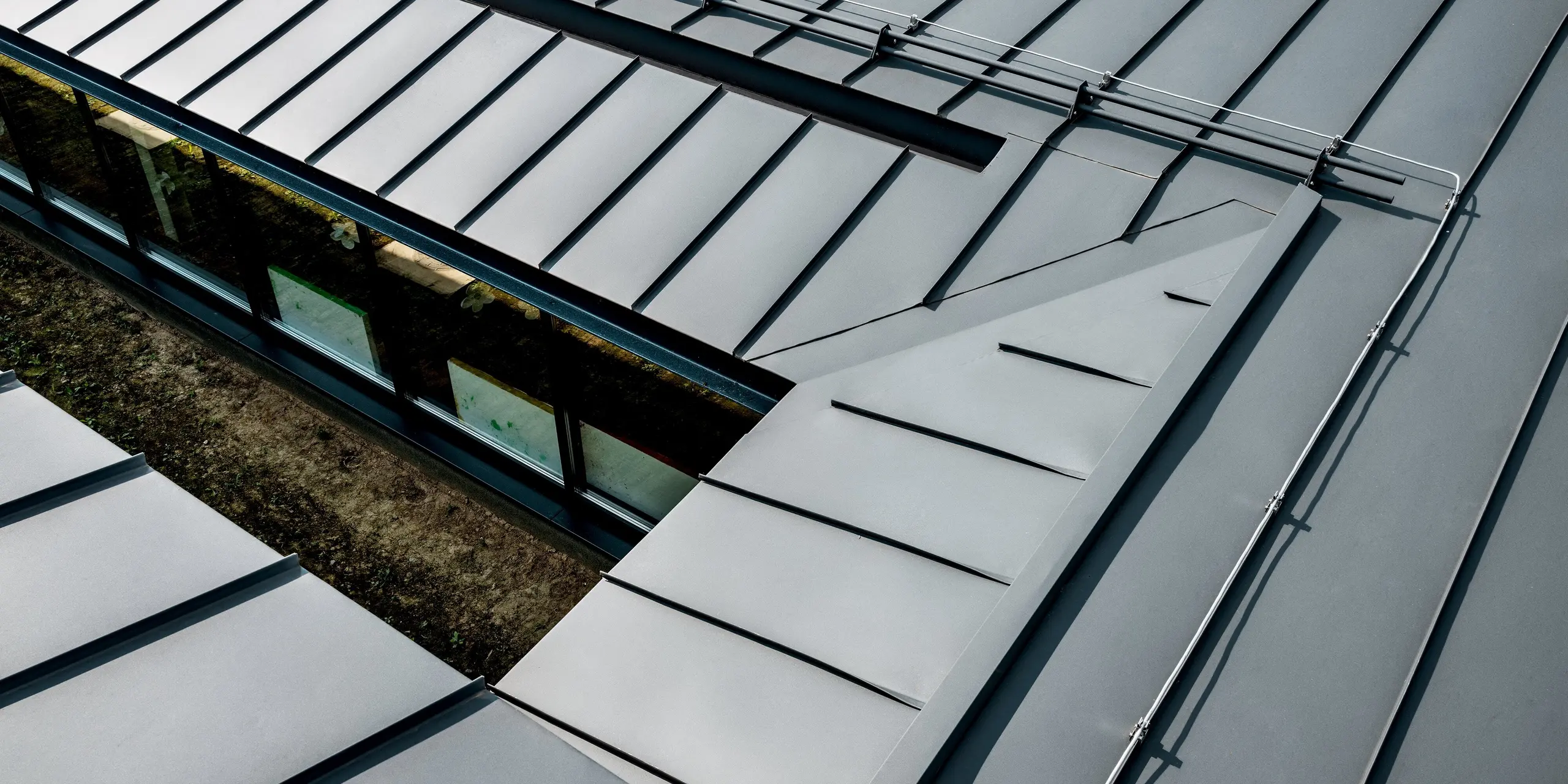 Detailaufnahme der präzise ausgeführten Stehfalz-Dachdeckung am Kindergarten Svarozic. Die klaren Linien und schmalen Stehfalze des Aluminiumdachs in P.10 Anthrazit zeigen die hochwertige Verarbeitung und moderne Ästhetik. PREFA Aluminium bietet zuverlässigen Witterungsschutz, hohe Langlebigkeit und eine elegante Oberfläche, die perfekt mit der Architektur harmoniert.