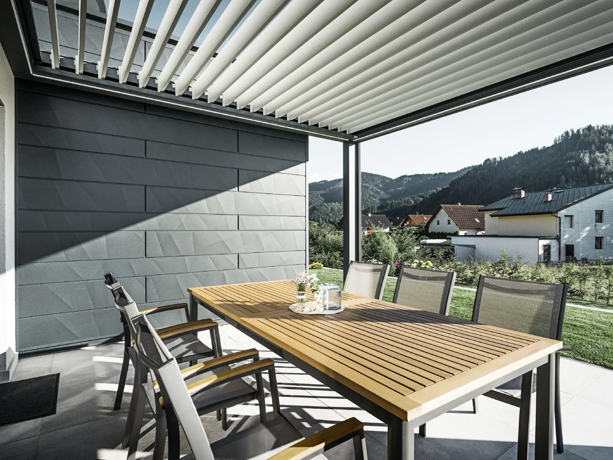 Terrazza coperta da pergolato a lamelle con arredi esterni; parete di fondo rivestita con pannelli per facciata Doga.X PREFA in colore antracite.