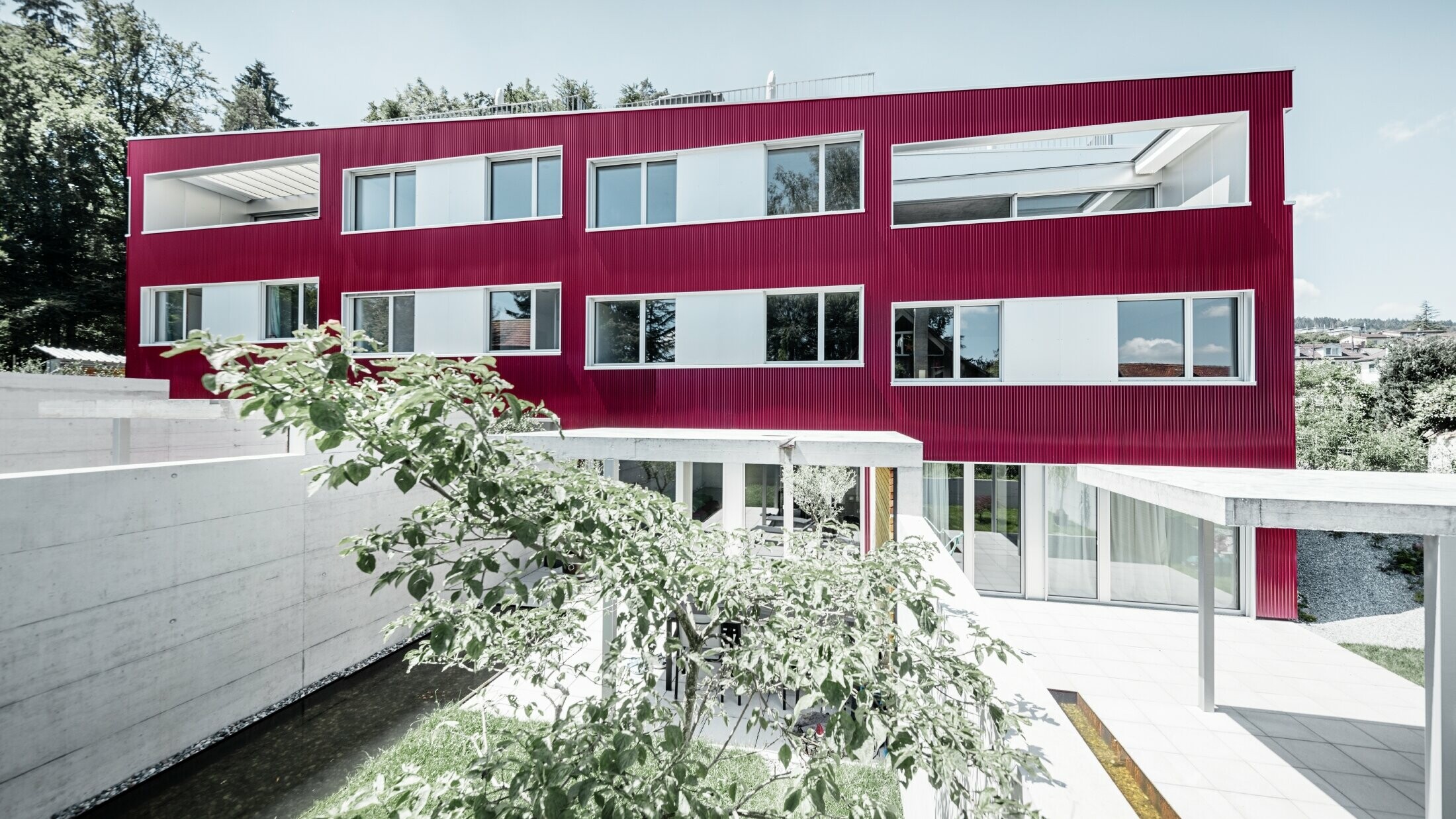 Complesso residenziale con tetto piano e balconi con facciata rosso vino con profilo ondulato PREFA 
