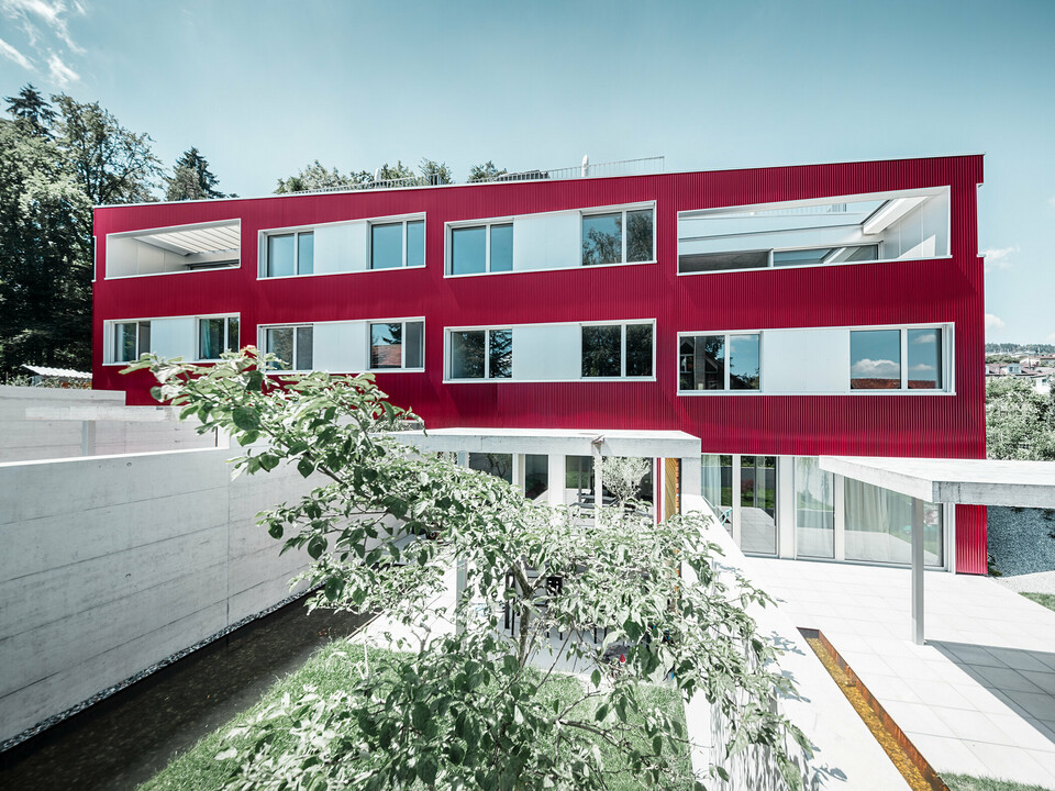 Wohnhausanlage mit Flachdach und Balkonen mit weinroter Fassade mit PREFA Profilwelle 