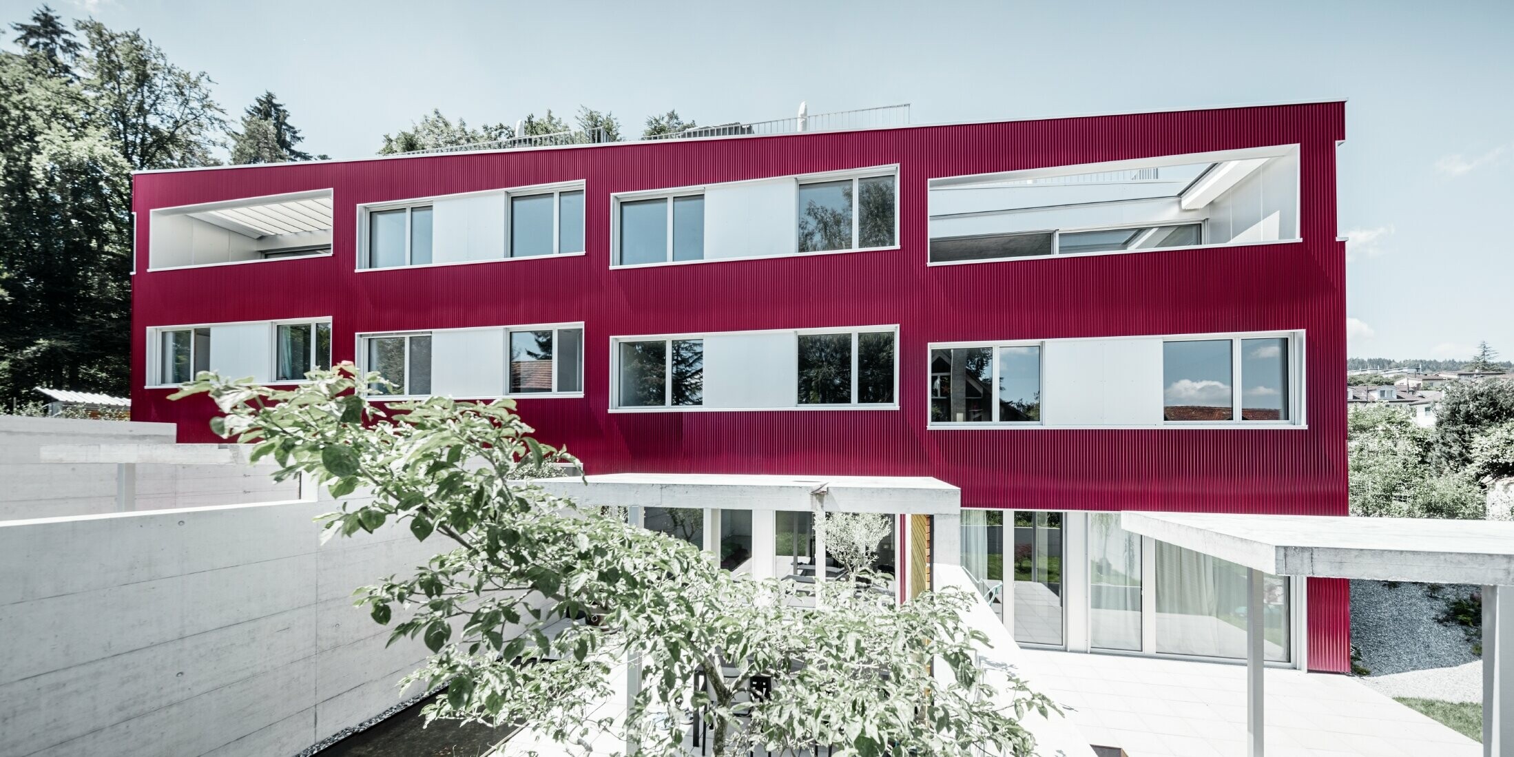 Complesso residenziale con tetto piano e balconi con facciata rosso vino con profilo ondulato PREFA 