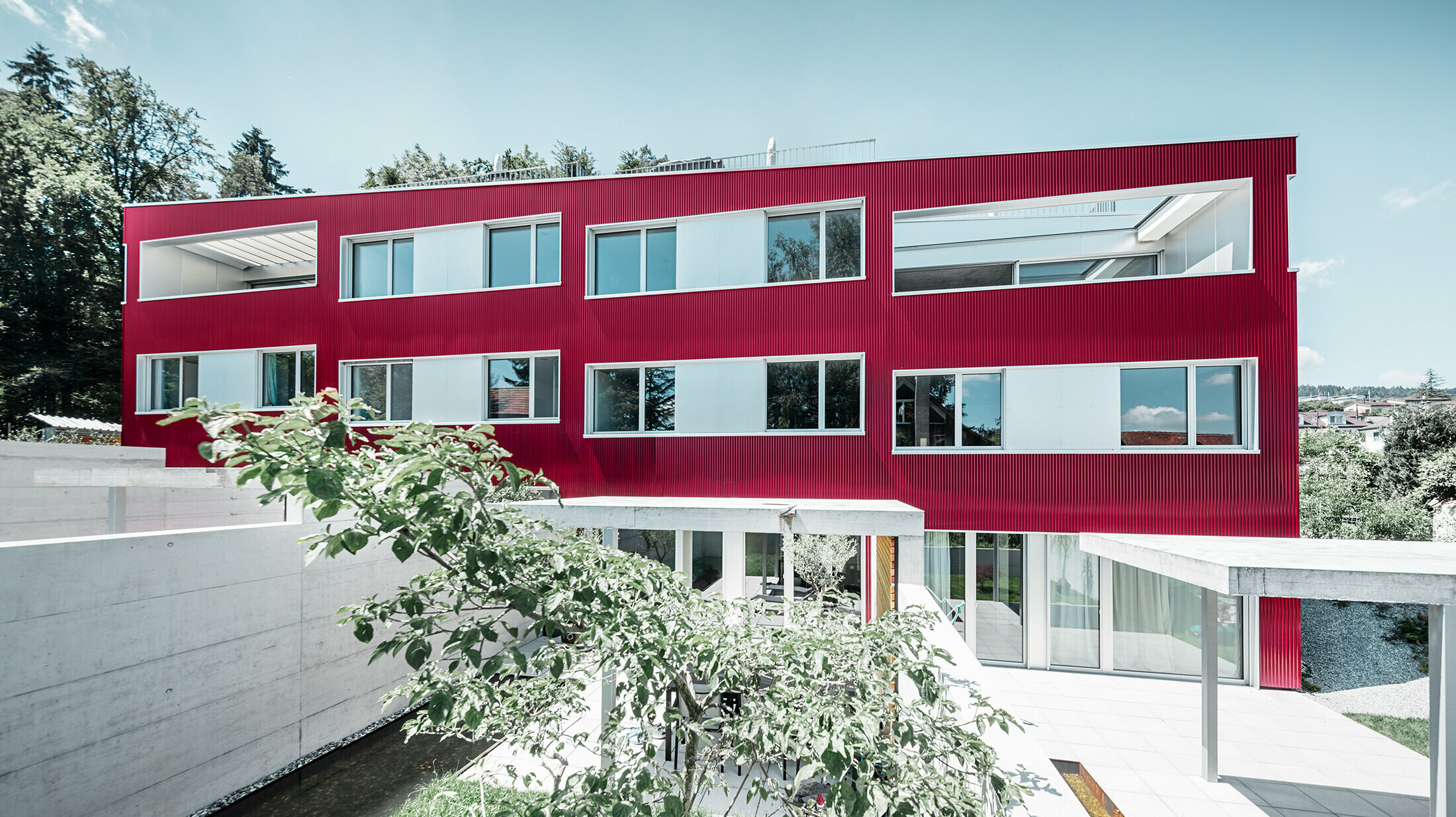 Wohnhausanlage mit Flachdach und Balkonen mit weinroter Fassade mit PREFA Profilwelle 