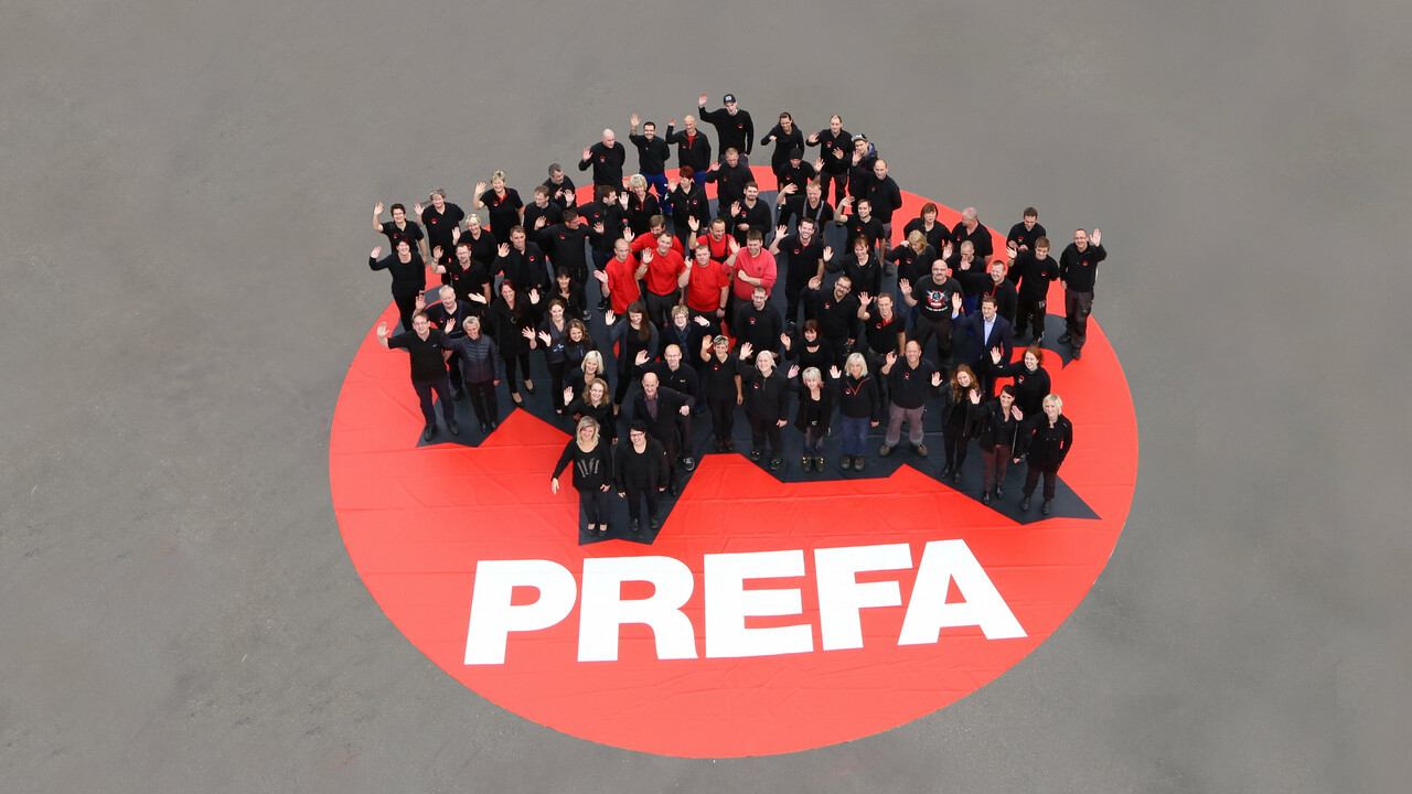 PREFA Team stehend auf einem roten PREFA Logo
