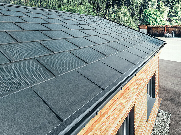 Tuile solaire PREFA en grand format, combinée avec le R.16 en noir, une gouttière carrée et une façade en bois de mélèze
