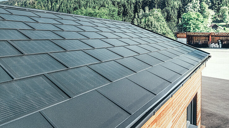 Tegola fotovoltaica PREFA in formato grande abbinata alla tegola R.16 in nero, canale quadro e facciata in legno di larice