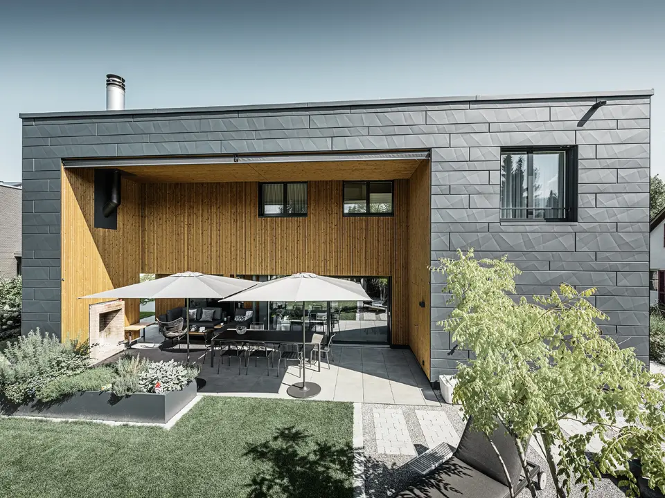 Modernes Einfamilienhaus mit Flachdach und Siding.X Fassade. Die Terrasse des Hauses ist mit schönen Sitzmöglichkeiten ausgestattet.