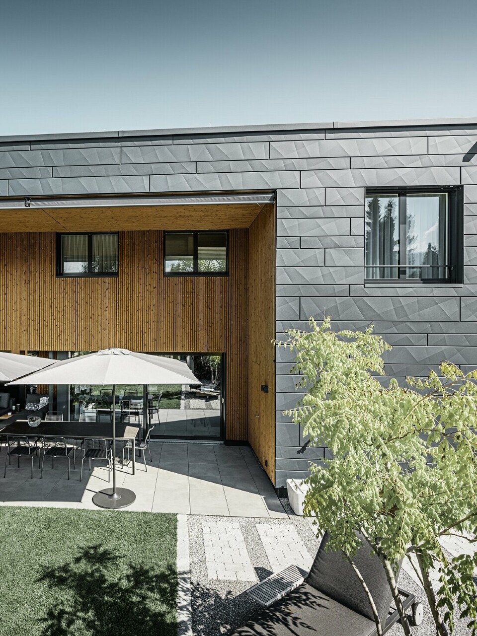 Modernes Einfamilienhaus mit Flachdach und Siding.X Fassade. Die Terrasse des Hauses ist mit schönen Sitzmöglichkeiten ausgestattet.