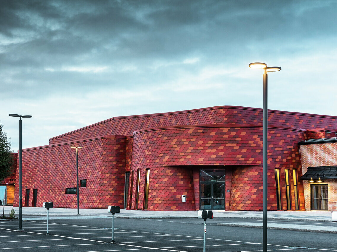 Prise de vue de la patinoire en Suède. La façade a été recouverte par des bardeaux PREFA dans les teintes P.10 rouge oxyde et deux teintes spéciale brun rouge et rouge brun.