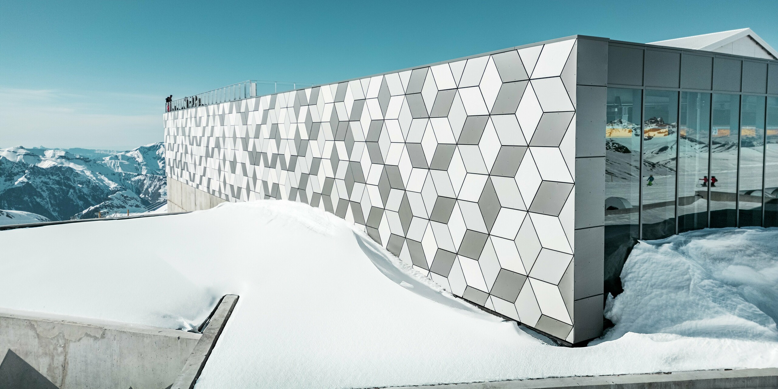 Die Bergstation der Seilbahn in Les Deux Alpes präsentiert sich mit einer atemberaubenden Fassade aus PREFABOND Aluminium-Verbundplatten, die in einem auffälligen Rautenmuster angeordnet sind. Die Platten in den Farben Weiß und Grau fügen sich nahtlos in die verschneite Berglandschaft ein und reflektieren das klare, alpine Licht. Diese innovative Fassadengestaltung vereint ästhetische Raffinesse und hohe Widerstandsfähigkeit gegen extreme Witterungsbedingungen.