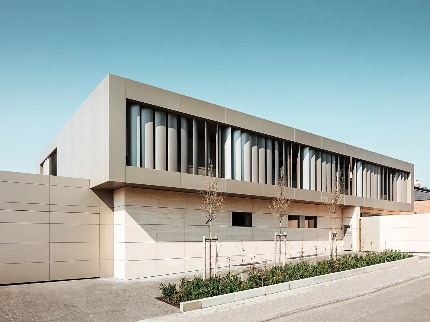 Straßenansicht, links Garage mit bronzefarbener Fassade, unten Steinfassade, oben bronzefarbene Aluminiumfassade mit Lamellen innen