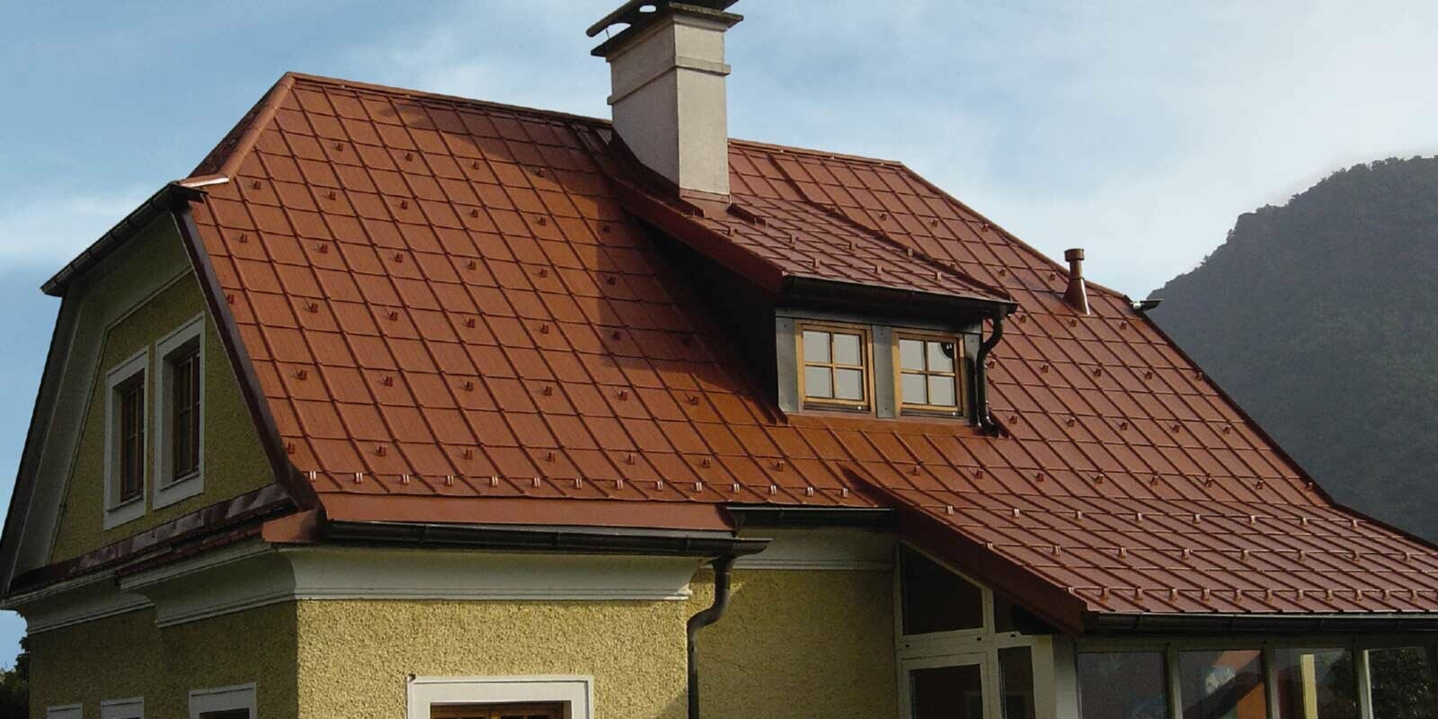 Maison individuelle avec toiture à deux pans en croupe et lucarne, fraîchement rénovée à l’aide de tuiles PREFA couleur rouge tuile