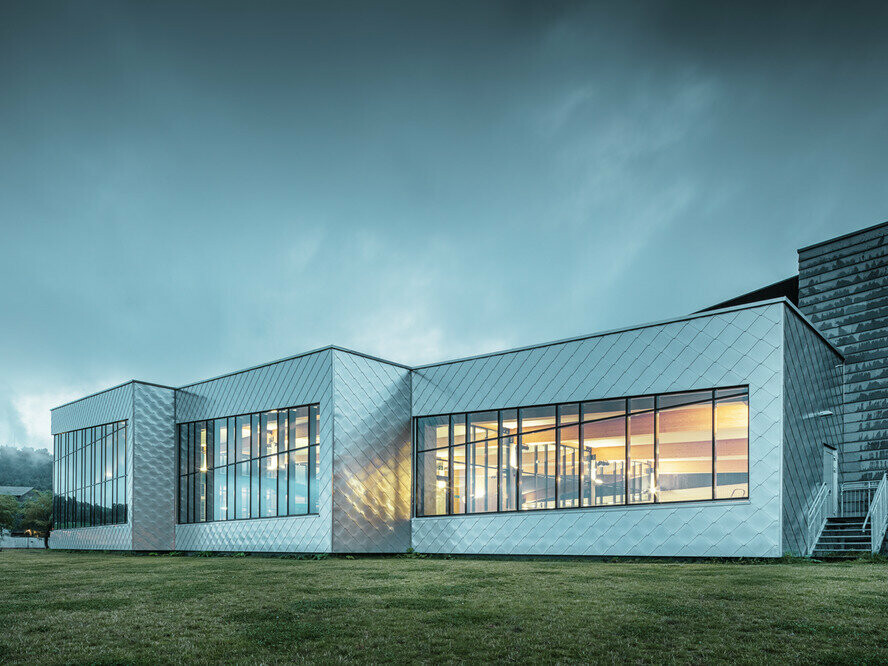 L'immagine mostra l'edificio polifunzionale di Oystese rivestito in Scaglia 44 x 44 colore alluminio naturale. Si vede un cielo scuro e nuvoloso all'orizzonte.