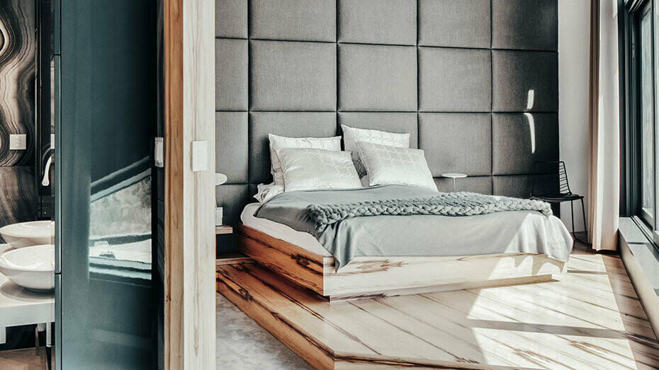 Ein Blick in das Schlafzimmer des Architektenhauses. Ein großes bequemes Bett schmückt das angenehme Ambiente, links ein kurzer Ausschnitt des modernen Badezimmers.