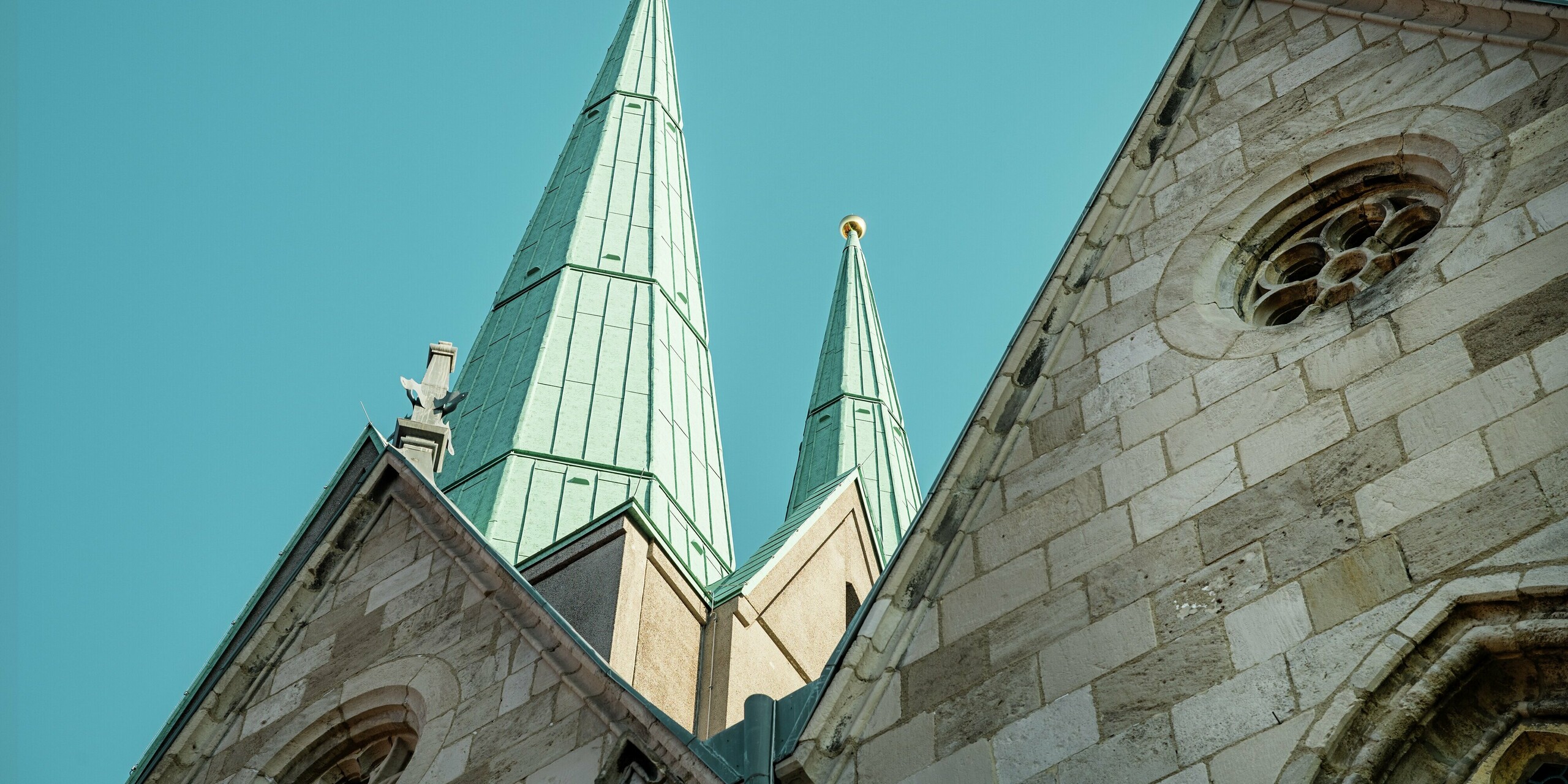 Vue d'ensemble des flèches magnifiquement restaurées de l'église Saint-Jean d'Ellrich. Les fines toitures en aluminium, recouvertes de PREFALZ P.10 vert de gris, s'élancent avec élégance vers le ciel et créent des accents architecturaux saisissants. Cette toiture métallique de haute qualité est sans entretien, extrêmement durable et idéale pour les bâtiments historiques à usage moderne.
