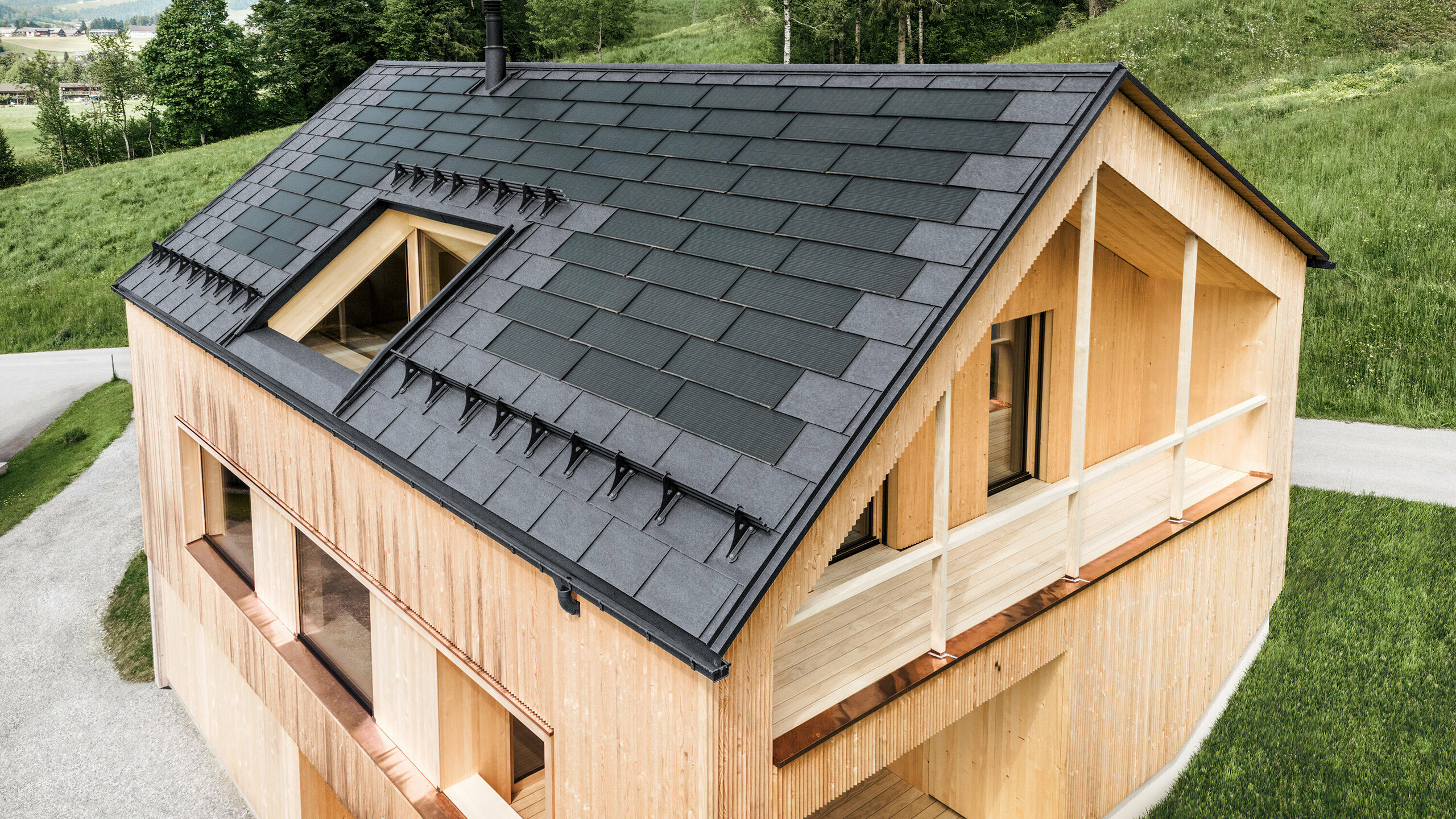 Maison individuelle dans la localité autrichienne d'Egg avec le panneau solaire de toiture PREFA et le panneau de toiture R.16 en gris pierre, combinés à une façade en bois