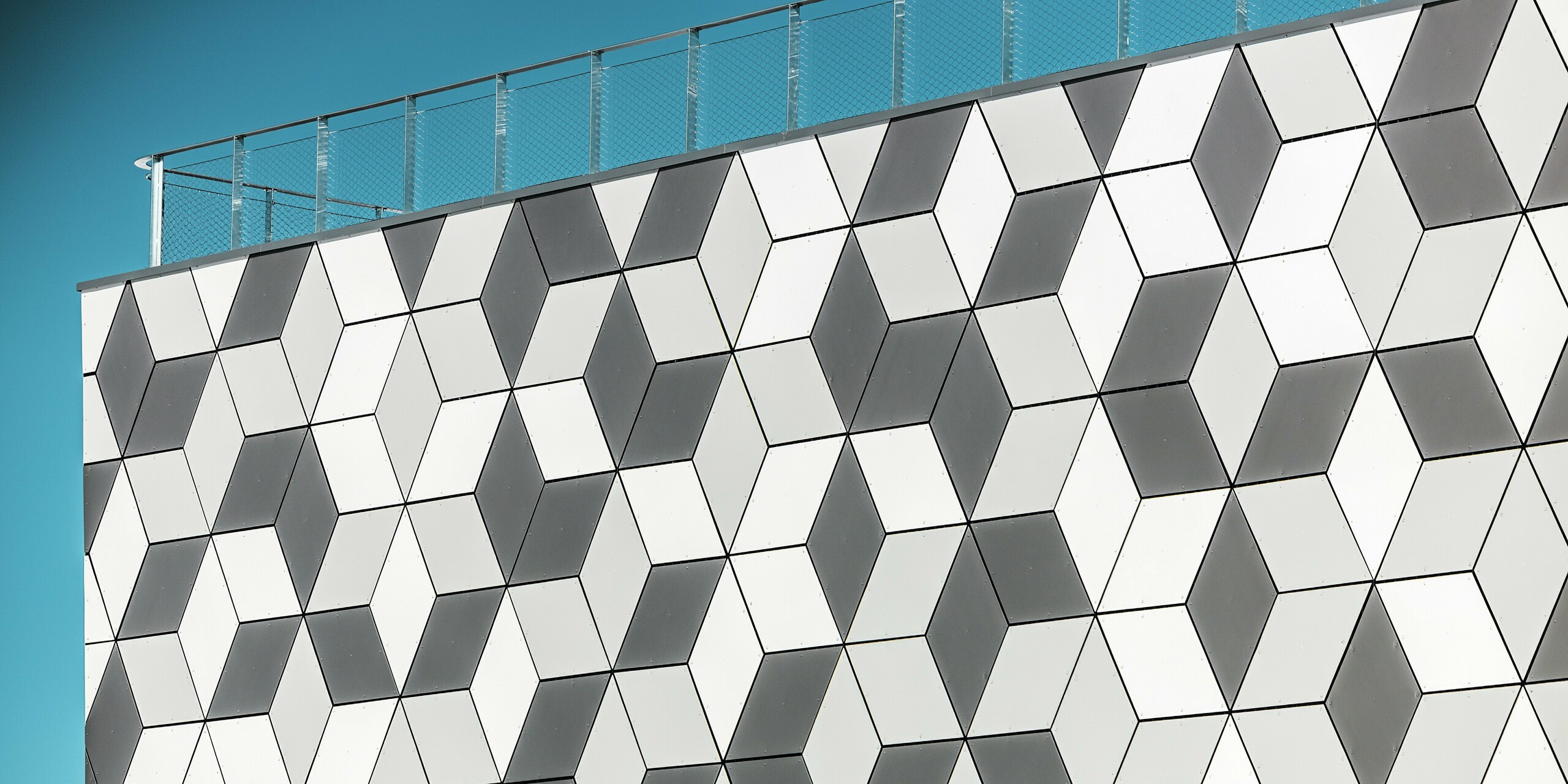 Die Fassade der Seilbahnstation in Les Deux Alpes besticht durch ihr dynamisches, geometrisches Design, das mit PREFABOND Aluminium Verbundplatten in Rautenform gestaltet wurde. Die präzise Anordnung der Platten in verschiedenen Weiß- und Grautönen erzeugt einen faszinierenden 3D-Effekt, der die minimalistische Architektur perfekt ergänzt. Dank der frostbeständigen und langlebigen Eigenschaften der Prefa-Aluminiumprodukte bleibt die Fassade auch bei extremen Bergwetterbedingungen dauerhaft ästhetisch und funktional.