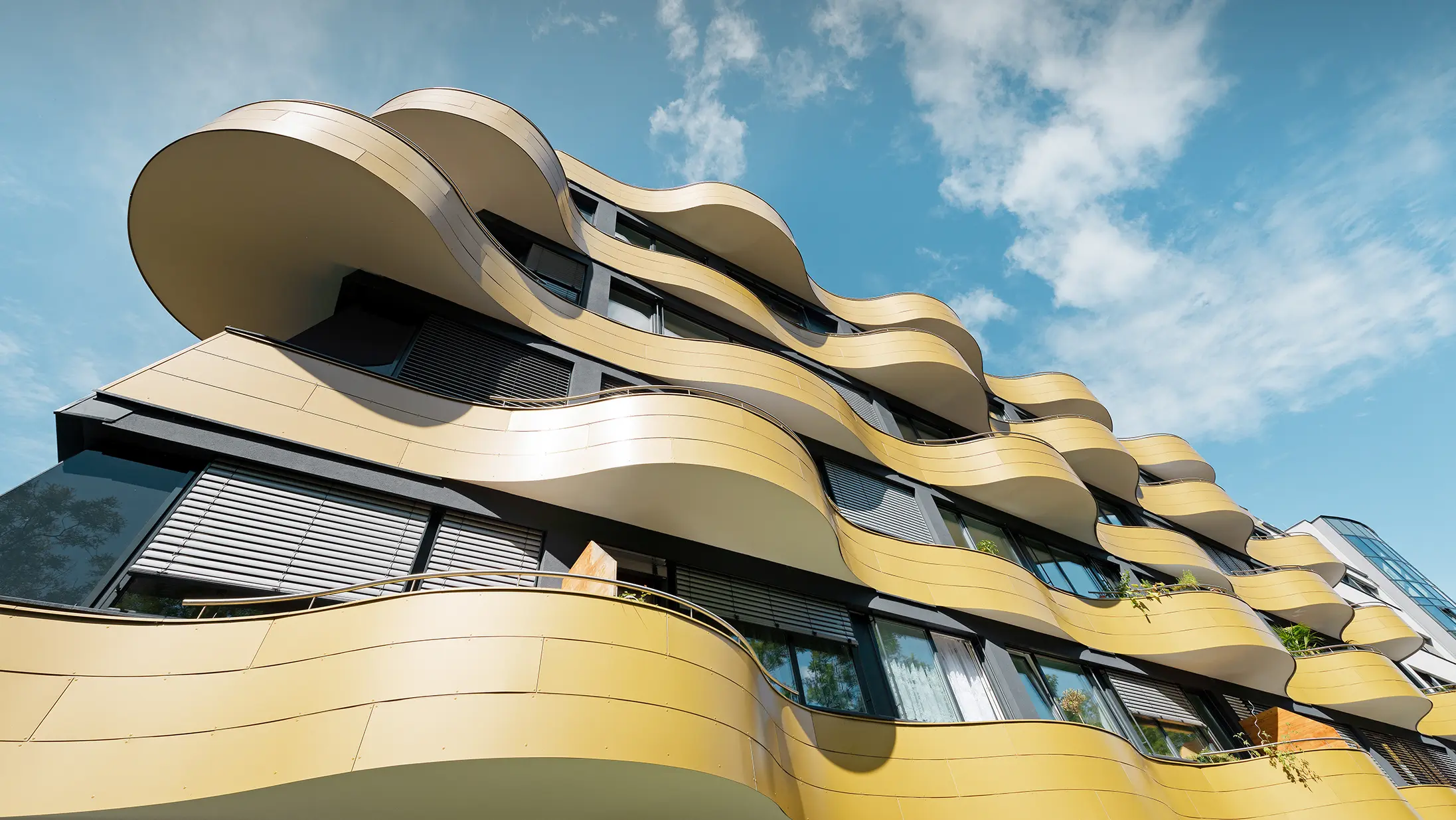 Froschperspektive auf die einzigartige Fassadengestaltung der Wohnhausanlage "Goldene Welle" in Graz. Die goldenen Balkone mit ihren speziellen Rundungen wurden mit Aluminium Verbundplatten bekleidet.