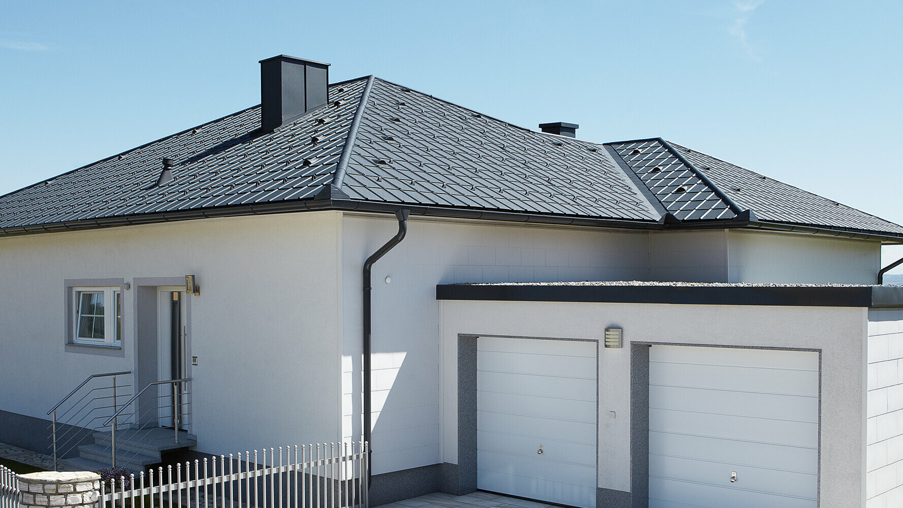 Bungalow ristrutturato con tetto a padiglione e rivestimento con tegola PREFA in antracite. Accanto c'è un box doppio.