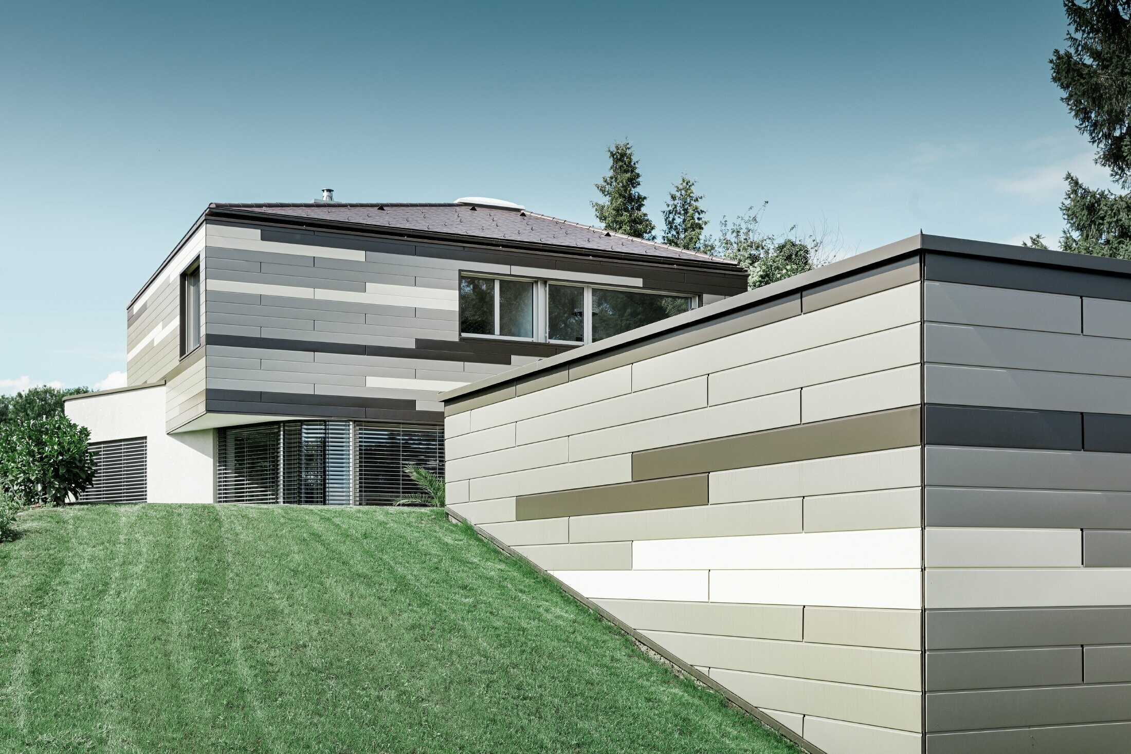 Casa unifamiliare moderna con copertura piana e terrazzo coperto con un'allestimento facciata personalizzato in alluminio in doghe in marrone, bronzo e avorio di PREFA