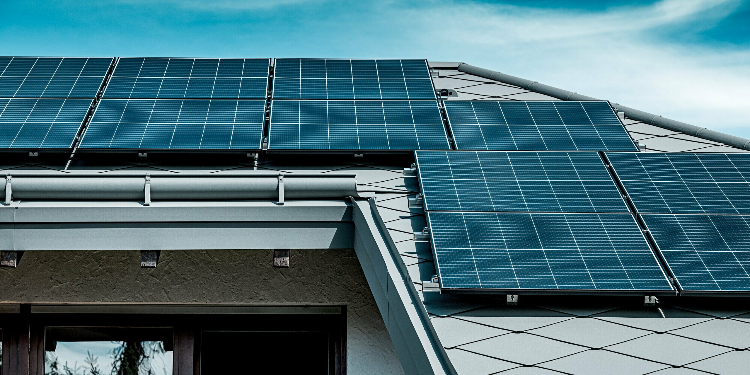 Nahaufnahme eines modernen Steildachs, das mit PREFA Dachrauten 44 × 44 in P.10 Hellgrau eingedeckt ist. Die präzise verlegte Rautenstruktur und die robuste PREFA Dachentwässerung bilden einen harmonischen Rahmen für die großflächig montierten Photovoltaik-Module. Der Kontrast zwischen den dunkel glänzenden Solarpaneelen und der hellgrauen Aluminiumdeckung erzeugt eine dynamische, technisch hochwertige Optik. Die langlebigen PREFA Materialien sorgen für maximale Stabilität, sichere PV-Befestigung und ein witterungsbeständiges, zukunftsfähiges Dachsystem.