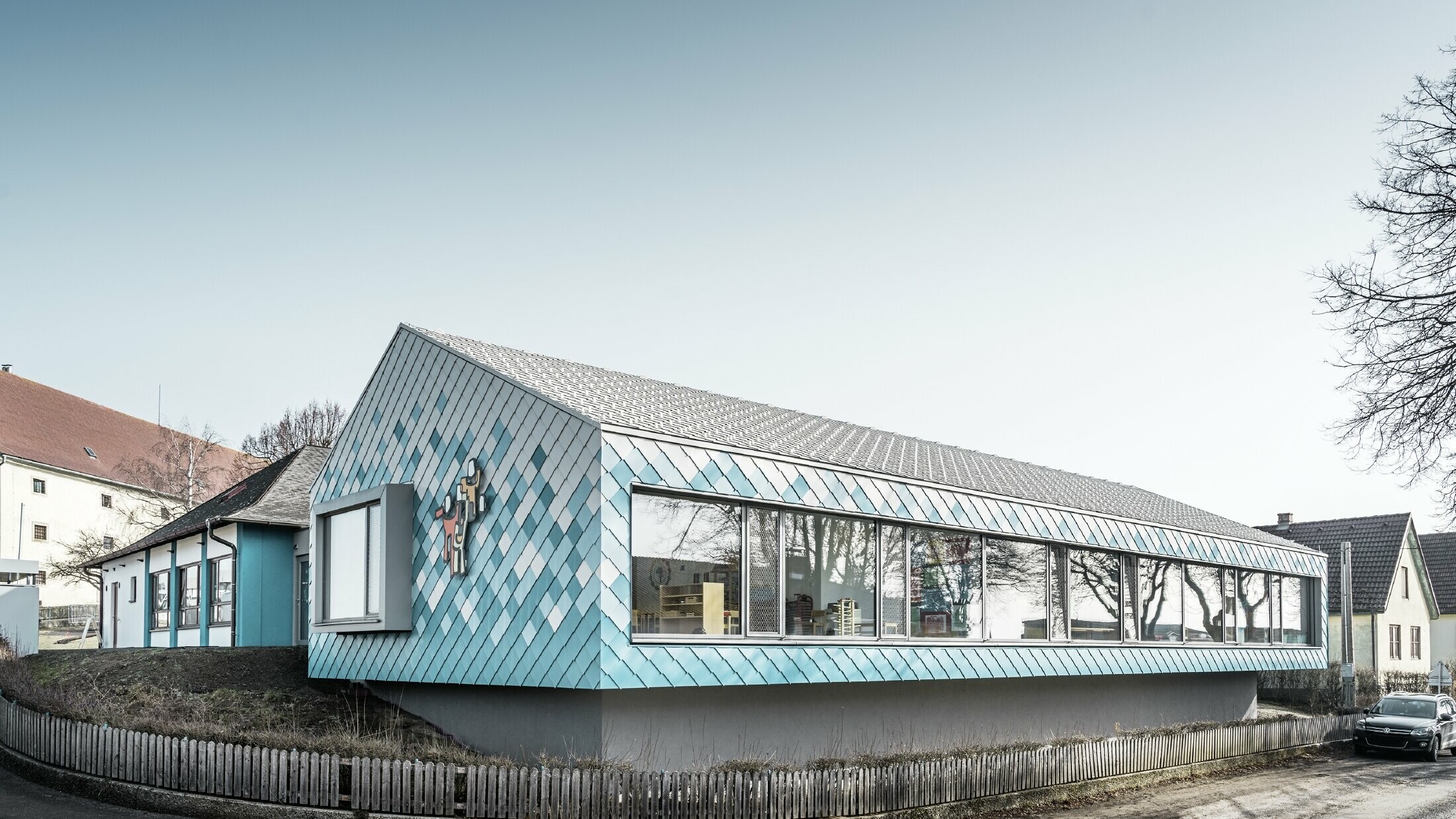 Per la progettazione della facciata della scuola materna è stato scelto il modello PREFA scaglia per facciata Alu 29 nei colori bianco puro, azzurro e turchese. Quest’ultimo è stato posato in un gradiente cromatico (blu in basso e bianco in alto).