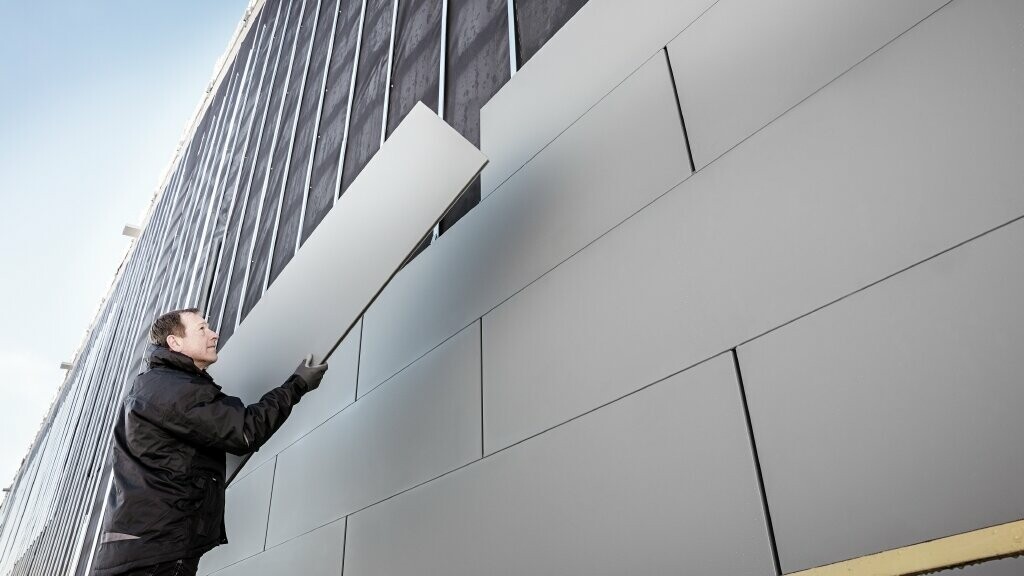 Prise de vue d'une façade partiellement terminée, revêtue de Sidings PREFA en largeur 500. Le couvreur est en train de poser une lame sur la façade. 