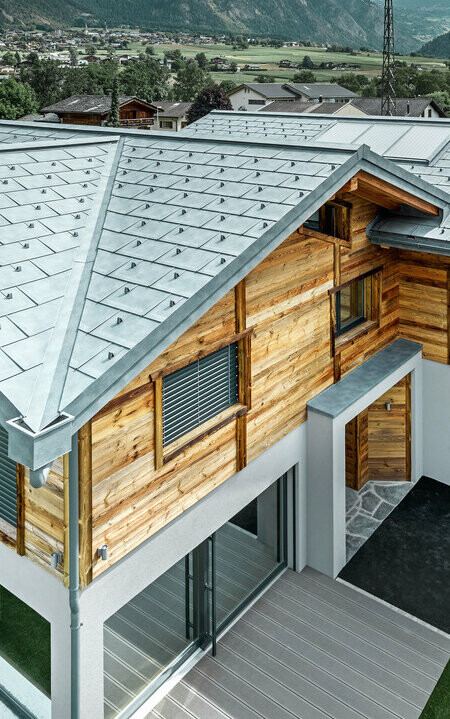 Chalet svizzero con tetto in alluminio di PREFA. La tegola R.16 è stata posata in grigio pietra. Al piano superiore è stata montata una facciata rustica in legno.
