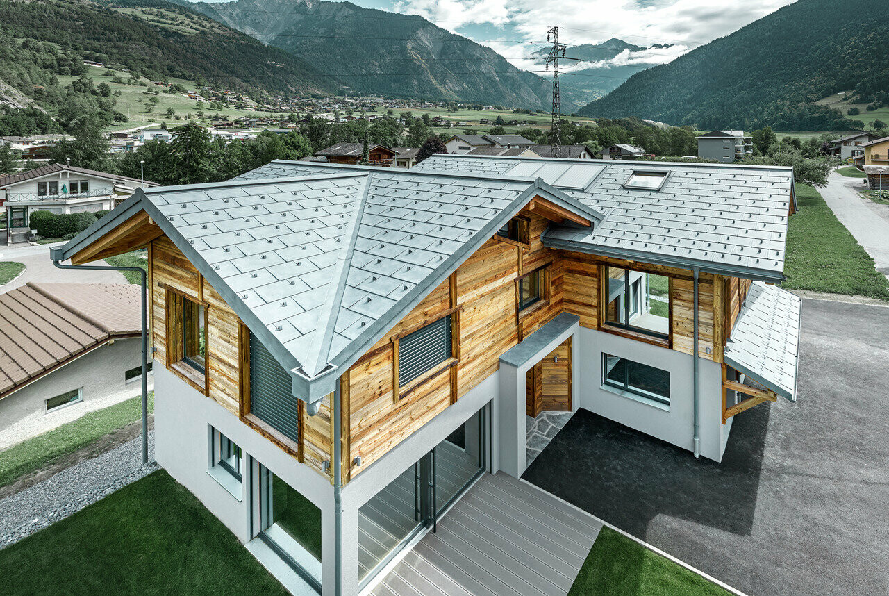 Chalet svizzero con tetto in alluminio di PREFA. La tegola R.16 è stata posata in grigio pietra. Al piano superiore è stata montata una facciata rustica in legno.