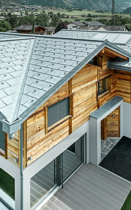 Schweizer Chalet mit einem Aludach von PREFA. Verlegt wurde die Dachplatte R.16 in Steingrau. In der oberen Etage wurde eine rustikale Holzfassade angebracht.