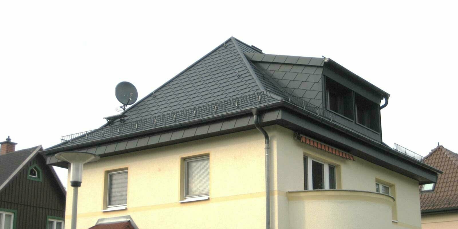 Ristrutturazione di un tetto a padiglione con scandole PREFA e abbaino, facciata gialla