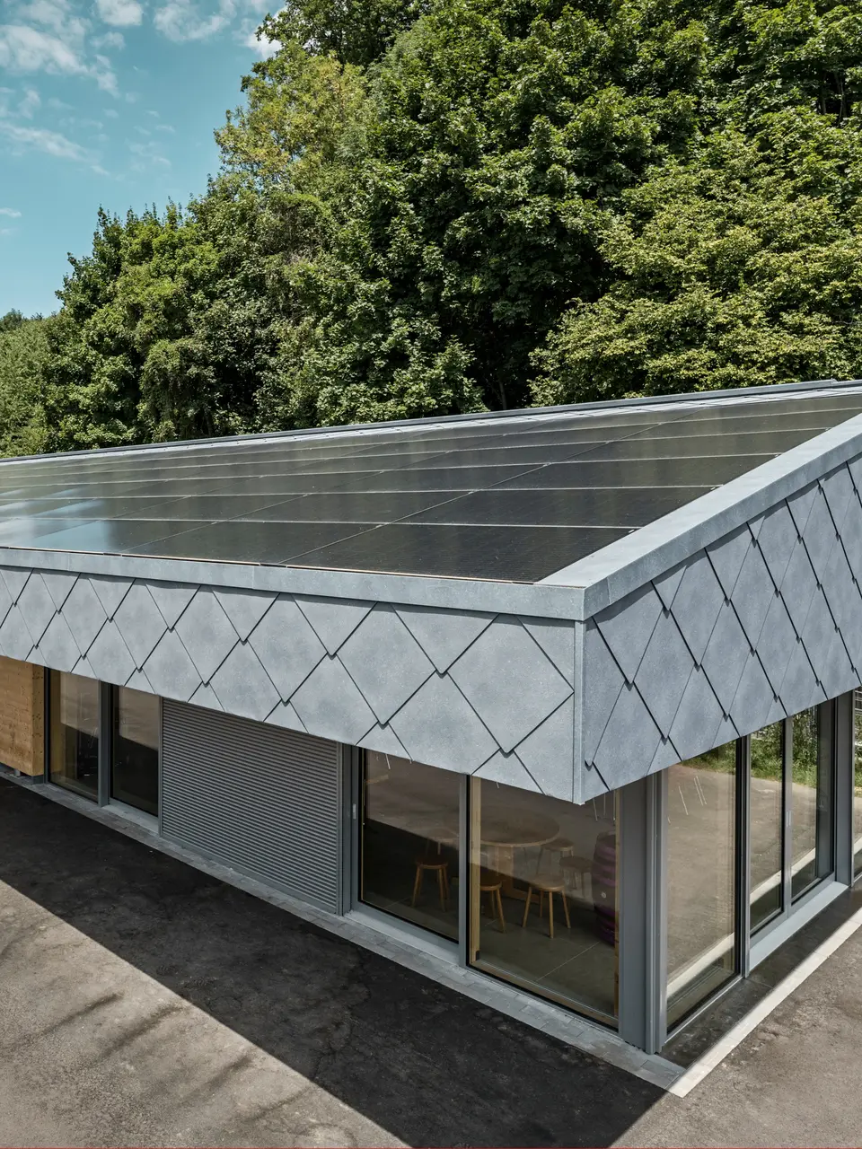 Ansicht von oben auf eine moderne Sportanlage in Prilly, Schweiz. Das Gebäude wurde mit mit langlebigen PREFA Dach- und Wandrauten 44x44 in der Farbe P.10 Steingrau ausgestattet. Die Rauten aus Aluminium sorgen für ein markantes Design, das perfekt mit der großflächig installierten Photovoltaikanlage harmoniert. Diese Kombination zeigt die innovative Verbindung von Funktionalität, Energieeffizienz und ansprechender Ästhetik, die für PREFA Aluminiumprodukte steht. Das Gebäude repräsentiert zukunftsorientiertes Bauen mit einem Fokus auf Nachhaltigkeit und Energieautonomie.