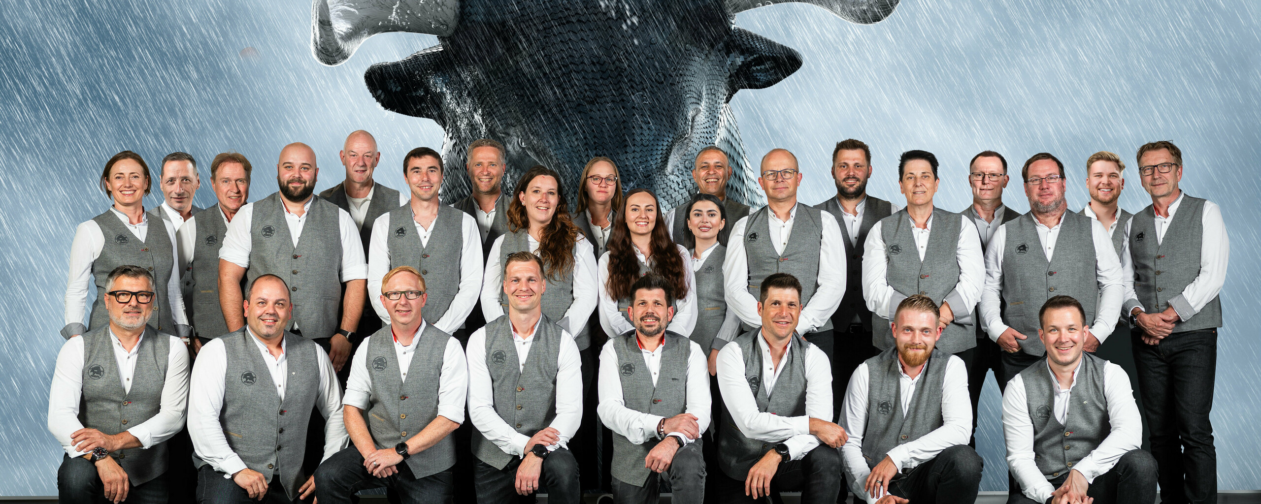 PREFA Mitarbeiter aus der Schweiz vor einer Leinwand, auf welcher der PREFA Stier zu sehen ist.