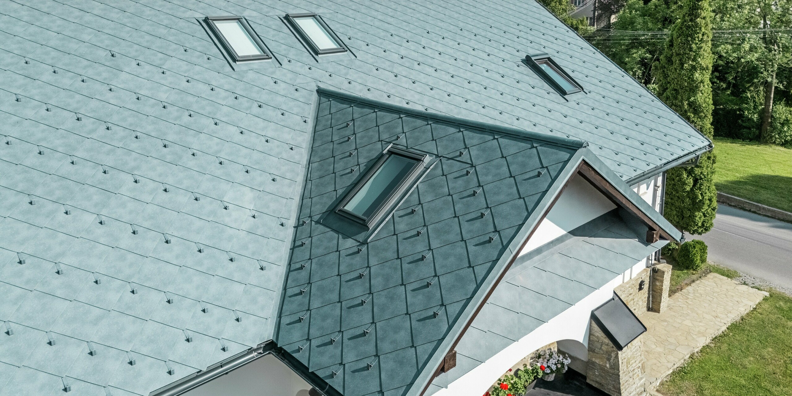 L'image présente la toiture rénovée d'une maison d'artisan historique à Klin, en Slovaquie, recouverte de losanges PREFA 44 x 44, couleur Gris Pierre P.10. Le motif losange saisissant confère au bâtiment une élégance et une modernité indéniables, tout en préservant son charme traditionnel. La structure uniforme de la couverture, l'harmonie des couleurs et les puits de lumière élégamment intégrés attirent particulièrement le regard. Outre son esthétique, la toiture en aluminium offre de nombreux avantages : elle est extrêmement durable, légère, résistante aux intempéries et à la corrosion. Cette rénovation constitue ainsi un projet durable qui allie parfaitement beauté et fonctionnalité.