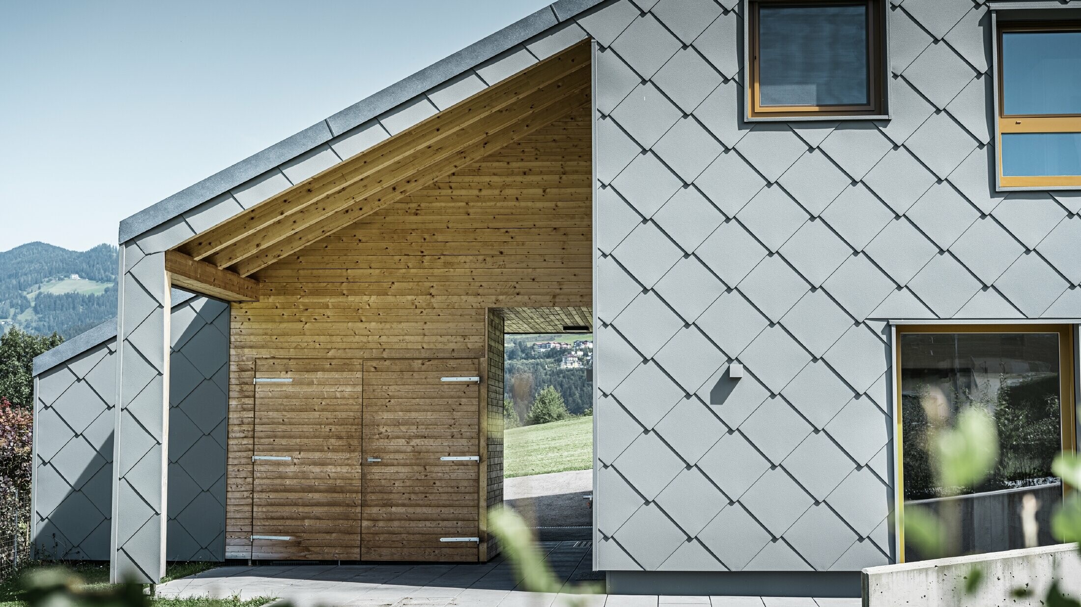 L’entrée couverte est faite de boiseries horizontales ; le reste de la façade est revêtu du losange de façade grand format PREFA en aluminium gris souris