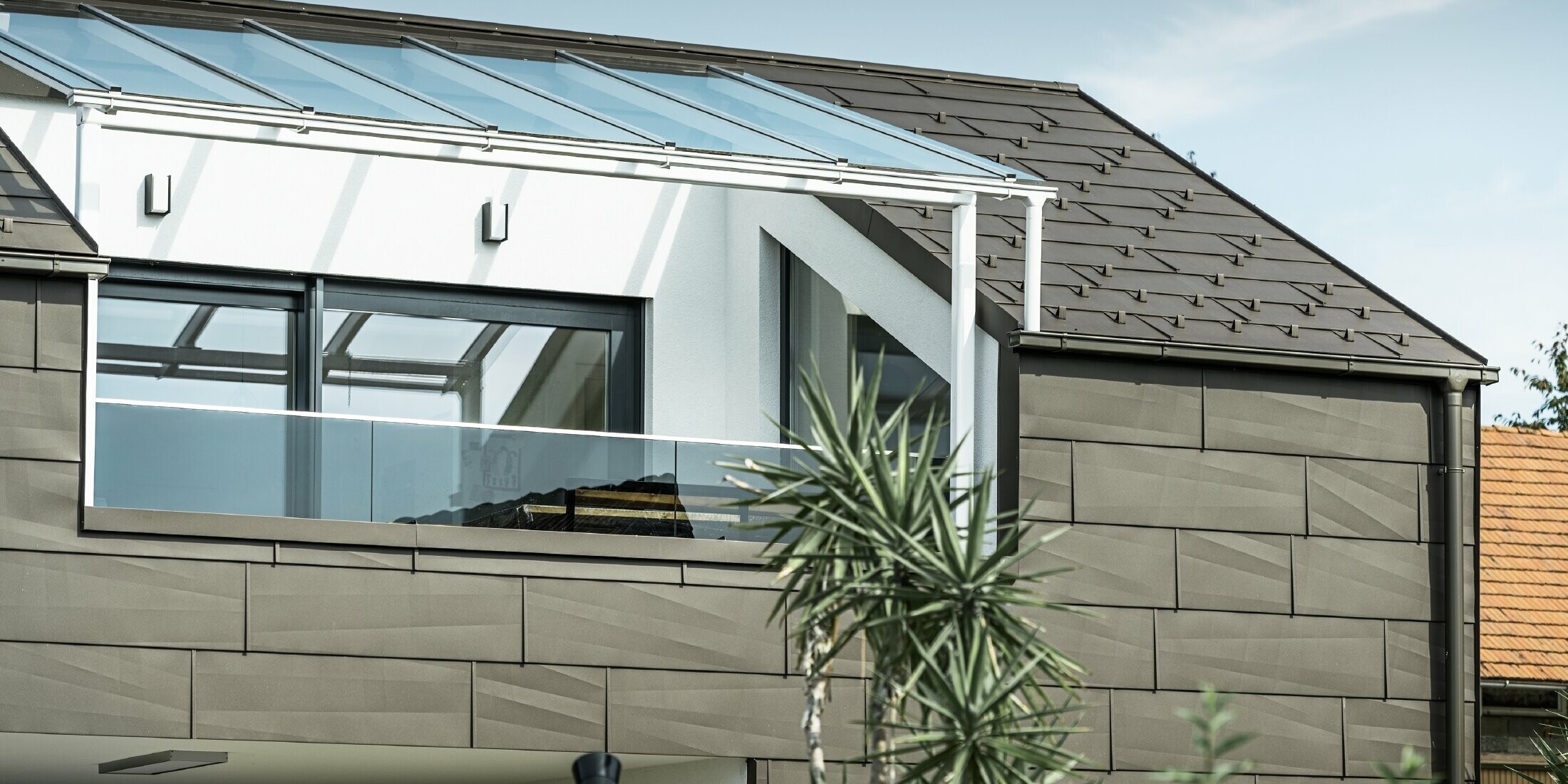 Extension avec terrasse de toit revêtue du système complet PREFA, le panneau de façade et de toiture FX.12 a été utilisé pour le toit et la façade. De plus, le système de gouttières est composé de la gouttière carrée PREFA avec tuyau de descente PREFA et accessoires complets, dans la couleur « brun ».