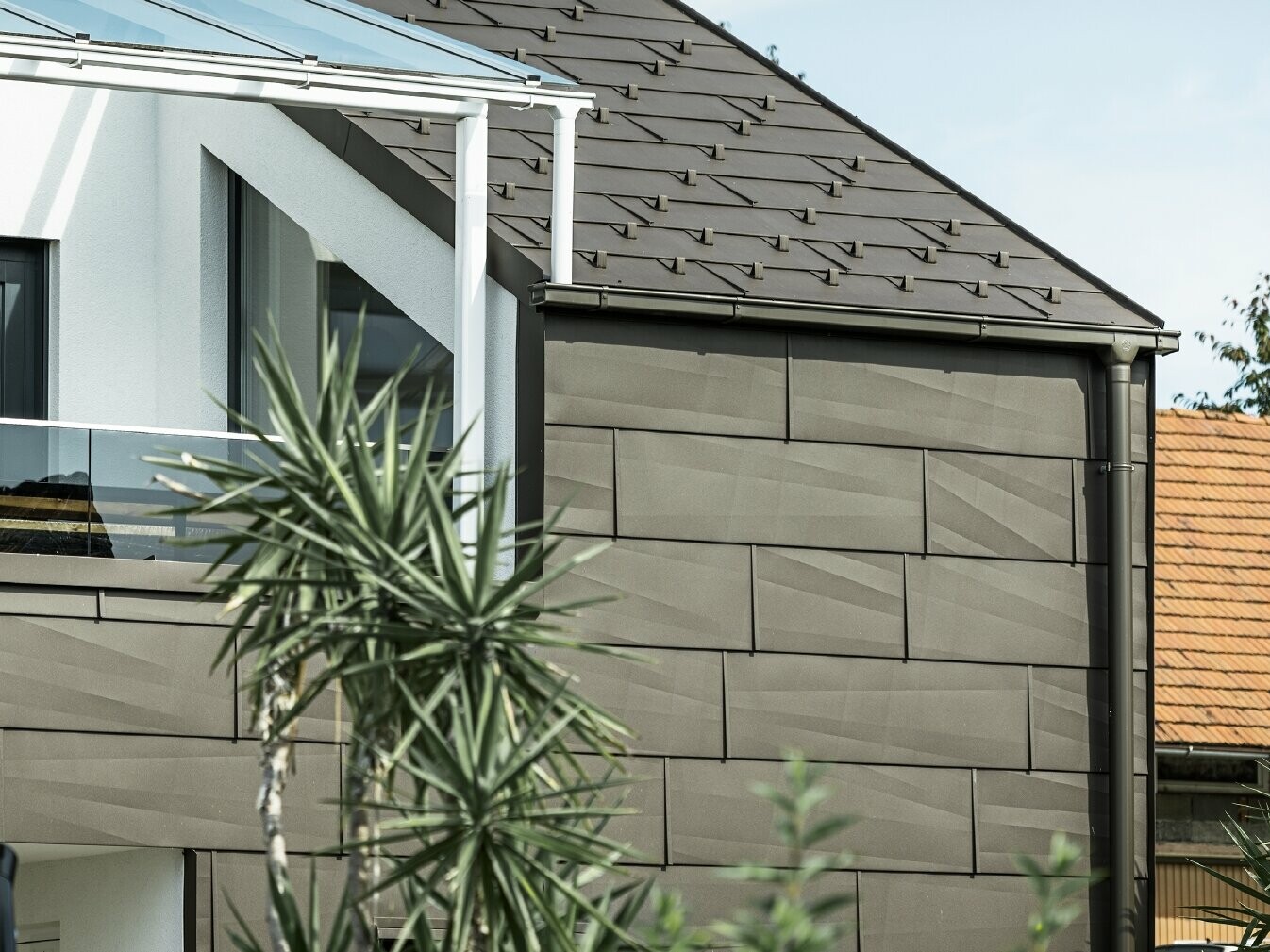 Extension avec terrasse de toit revêtue du système complet PREFA ; pour le toit et la façade, le choix s'est porté sur le panneau de toiture et de façade FX.12 PREFA. Pour l'écoulement des eaux de pluie, le choix s'est également porté sur la gouttière carrée PREFA avec tuyau de descente PREFA et accessoires complets en brun.
