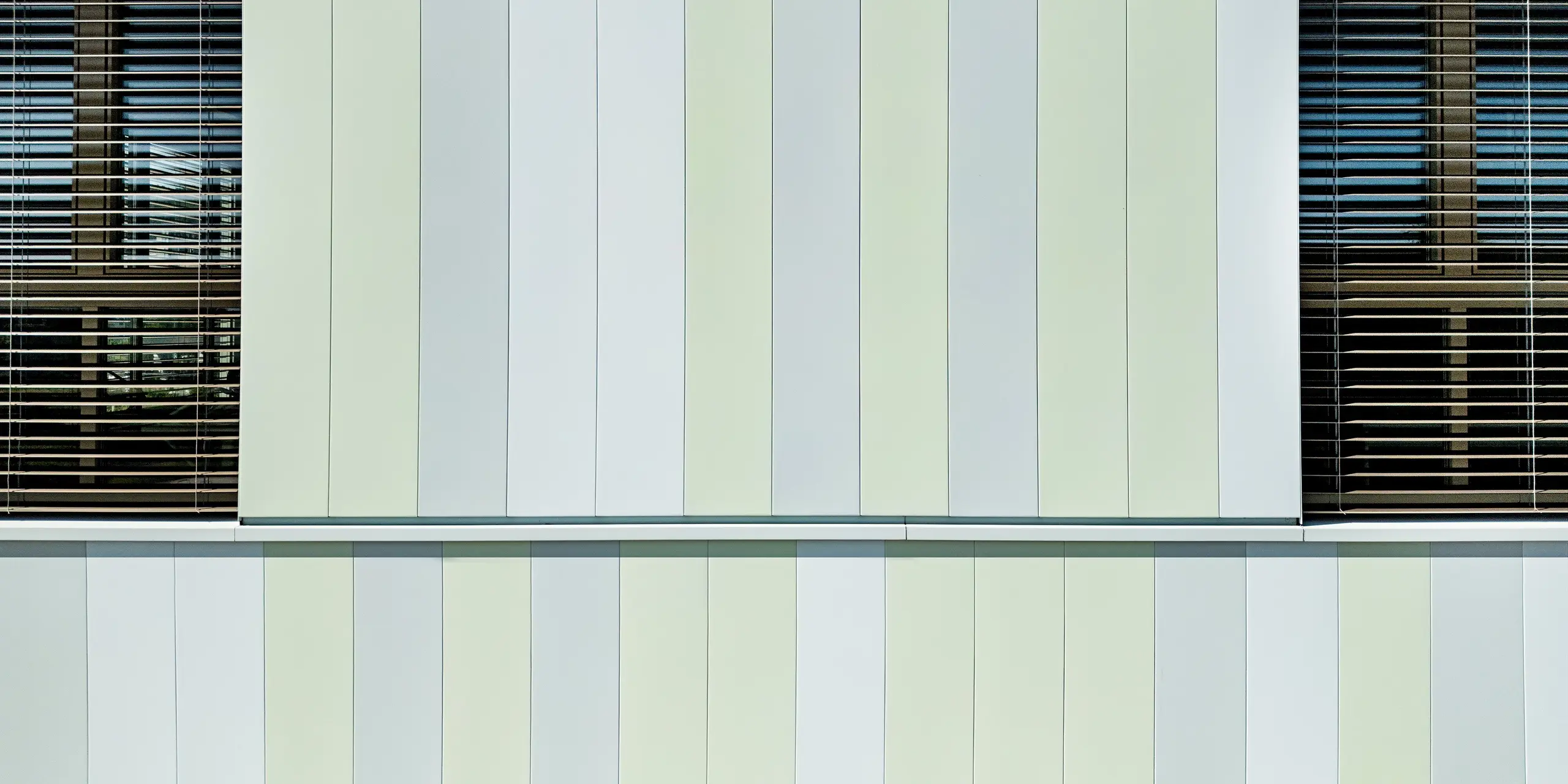 Die Fassade der AHS Reininghaus in Graz beeindruckt durch die stilvolle Kombination von PREFA Sidings in Sonderfarben. Die vertikalen Aluminiumprofile in sanften Grün- und Weißtönen verleihen dem Gebäude ein modernes, frisches Erscheinungsbild. Besonders auffällig sind die perfekt abgestimmten Fensterrahmen und Jalousien, die das lichtdurchflutete Design der Fassade ergänzen. Die Verwendung von PREFA Produkten sorgt für eine besonders langlebige, pflegeleichte und wetterbeständige Oberfläche, die gleichzeitig ästhetische Akzente setzt. Diese moderne Fassadengestaltung trägt nicht nur zur optischen Aufwertung des Gebäudes bei, sondern sorgt auch für nachhaltige Energieeffizienz und Schutz vor Umwelteinflüssen.