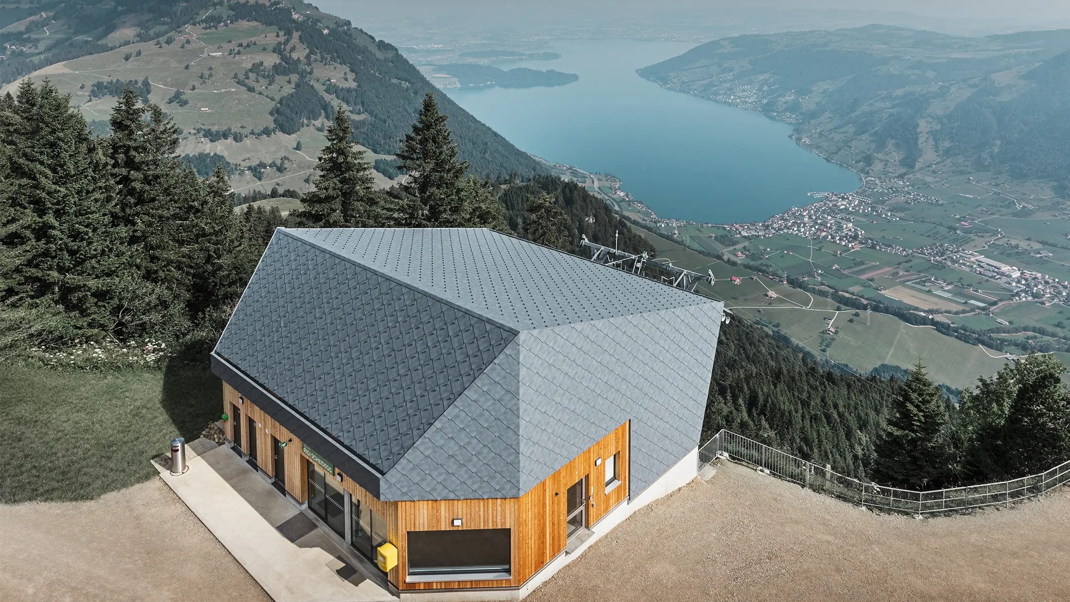 Vue aérienne de la gare d’arrivée du téléphérique du Rigi Scheidegg recouverte de losanges de façade 44 × 44 PREFA couleur P.10 gris pierre et bois.