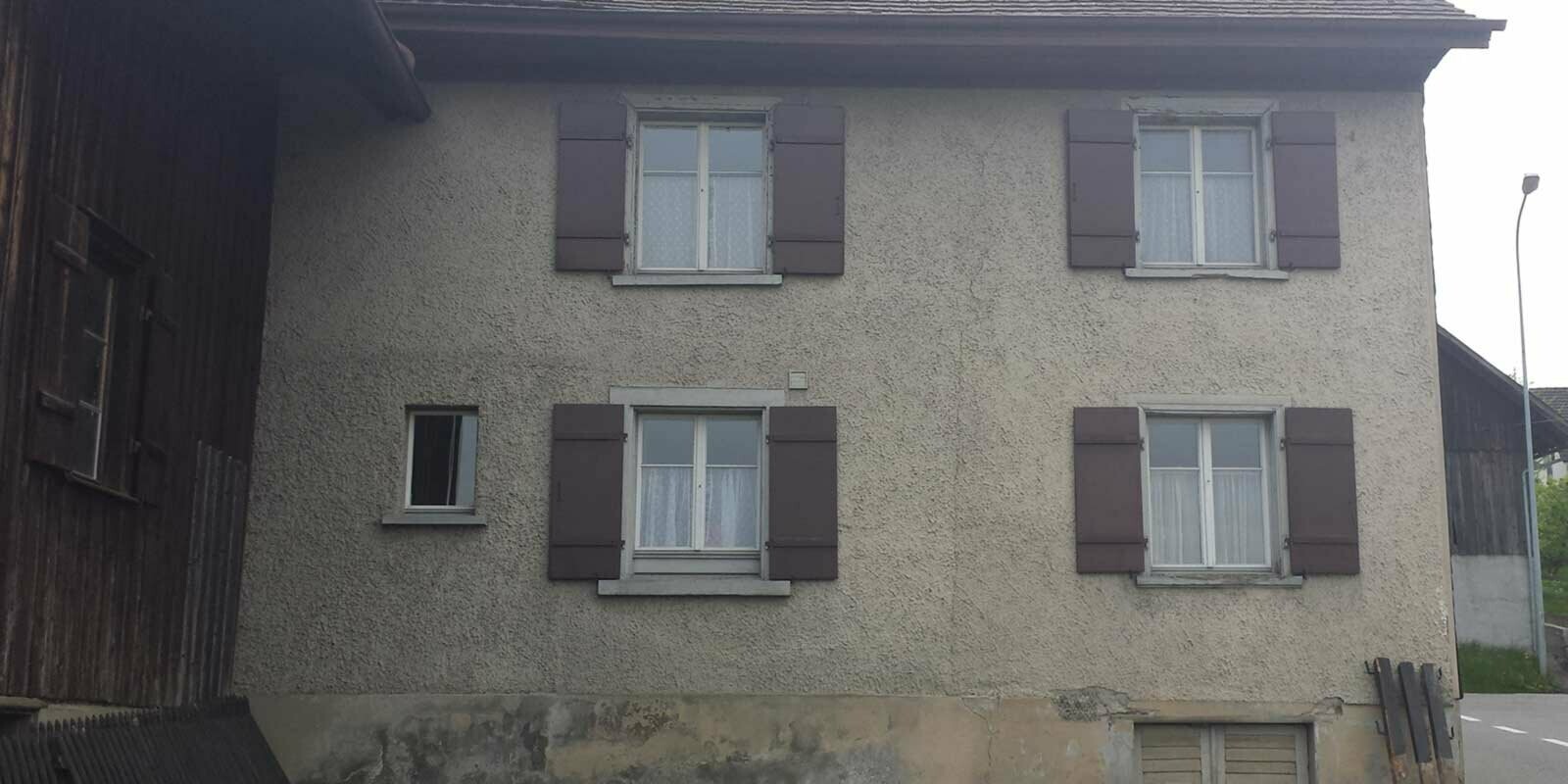 Maison avant la rénovation de façade à l’aide de losanges de façade PREFA, fenêtres dotées de volets rouges