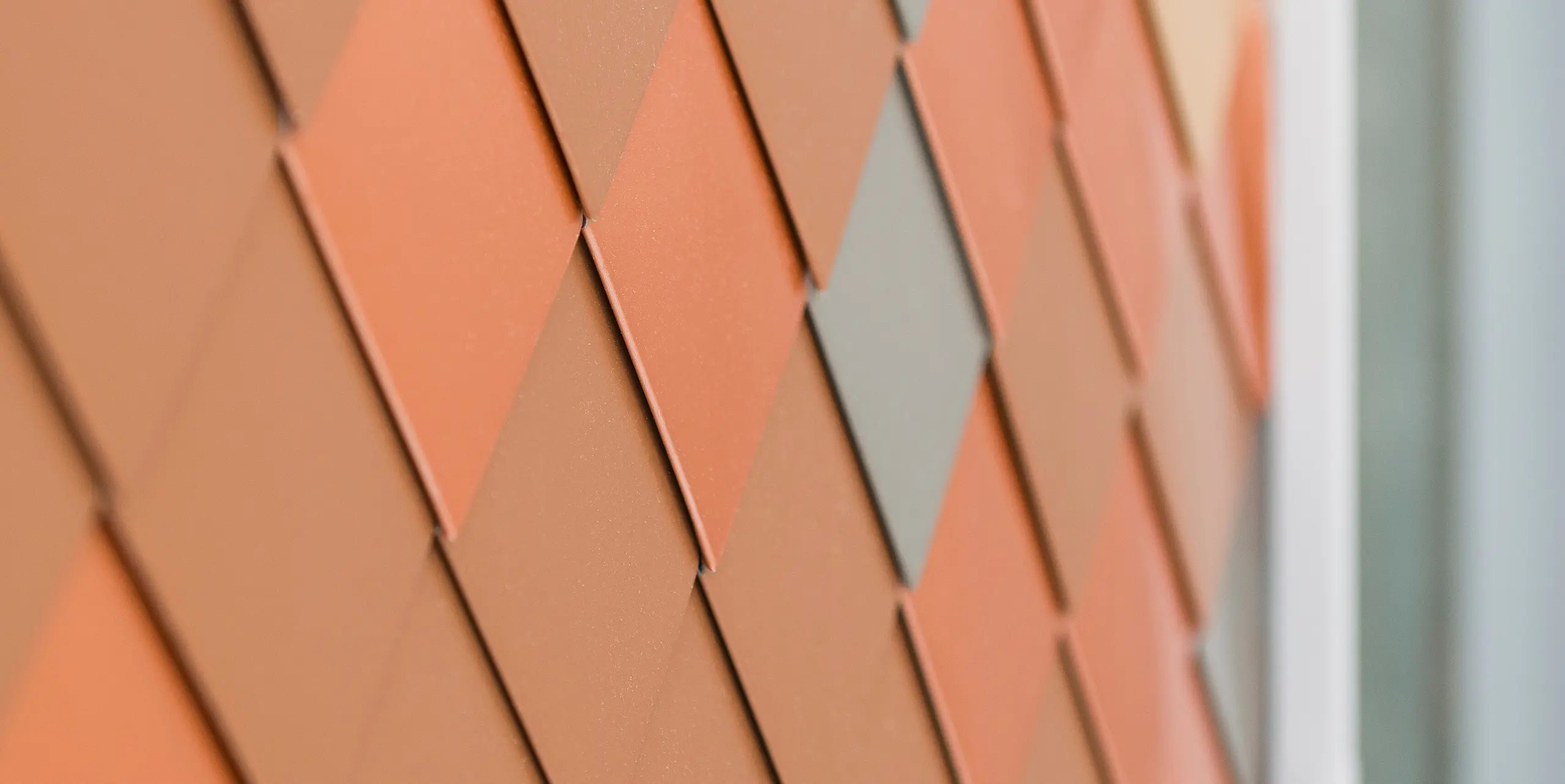 Detailansicht einer modernen Aluminiumfassade von PREFA mit einem geometrischen Muster in verschiedenen Farbtönen. Die kleinen Aluminiumteile aus FALZONAL sind diamantförmig angeordnet und erzeugen eine dreidimensionale Optik, die Struktur und Farbtiefe betont