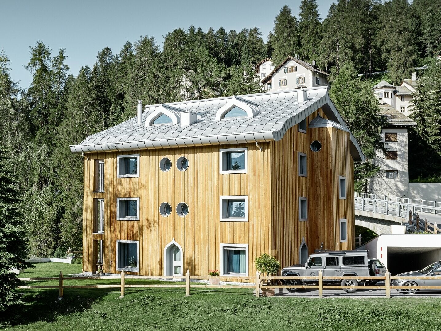 Wohnhausanlage in St. Moritz mit Holzfassade und Aluminiumdach mit geschwungener Traufe in silbermetallic