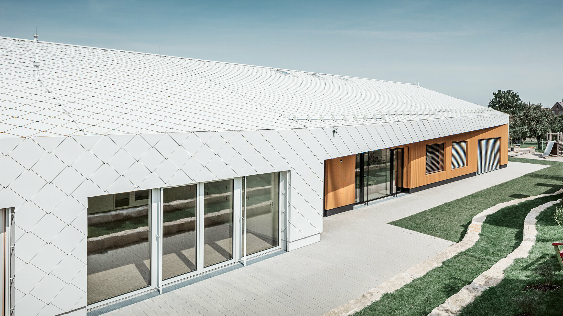 Jardin d’enfants revêtu du losange de toiture et de façade 44 de PREFA, en blanc Prefa ; la surface du toit et la façade ne font qu'un ; grandes surfaces vitrées