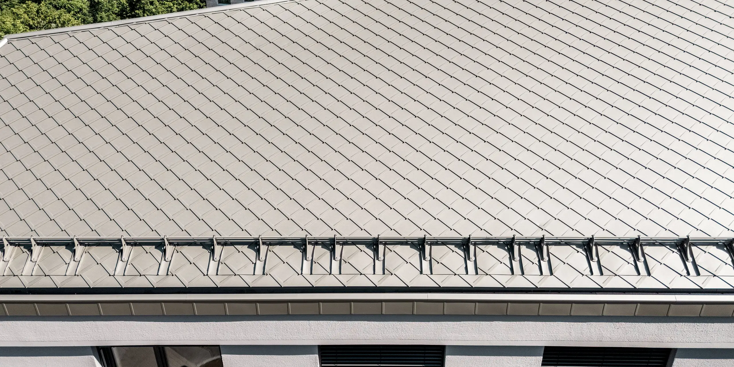 Die detailreiche Nahaufnahme des Daches der Sparkasse Blaubeuren zeigt die präzise Verlegung der PREFA Dachrauten 44 × 44 in Bronze. Das gleichmäßige Rautenmuster verleiht der großzügigen Dachfläche eine elegante, strukturierte Optik. Ein integriertes Schneefangsystem ergänzt die Dachgestaltung. Die leichten, langlebigen und witterungsbeständigen Aluminiumrauten überzeugen durch Ästhetik und Funktionalität.