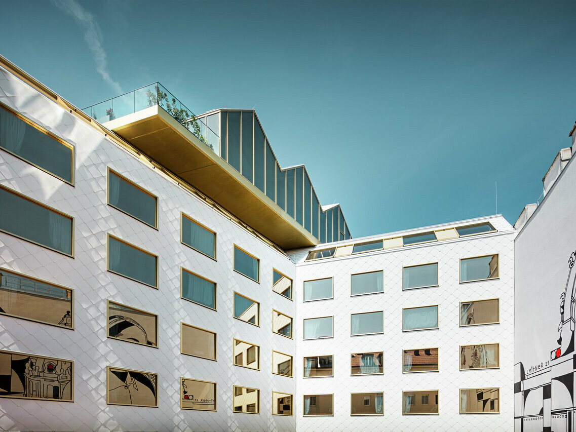 Vista prospettica dell'hotel "THE ROCK Radisson RED Vienna" di Vienna, caratterizzato dall'innovativa facciata in alluminio PREFA con tetto e pareti a rombi 44 × 44 in P.10 bianco puro. Le finestre disposte in modo irregolare con vetri a specchio riflettono dinamicamente l'ambiente circostante.