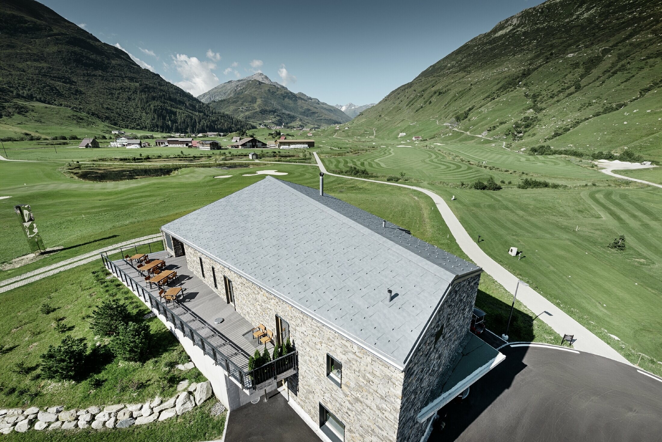 Il moderno punto di ritrovo del campo da golf a Andermatt con una facciata in pietra e il pannello per coperture FX.12 PREFA in alluminio in grigio pietra