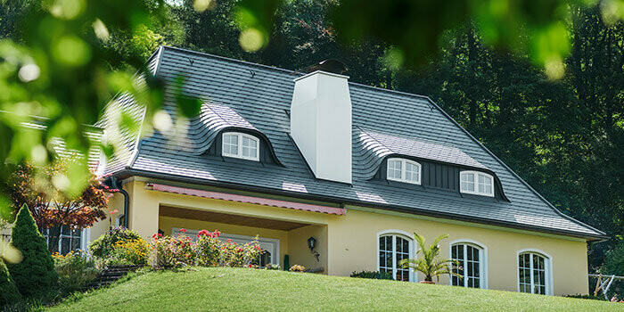 Casa monofamiliare con nuovo tetto ristrutturato con scandole PREFA color antracite con abbaini arrotondati (abbaini a pipistrello) e camino bianco.